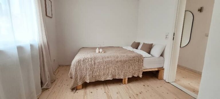 Schlafzimmer mit Bett vor heller Wand und offener Tür